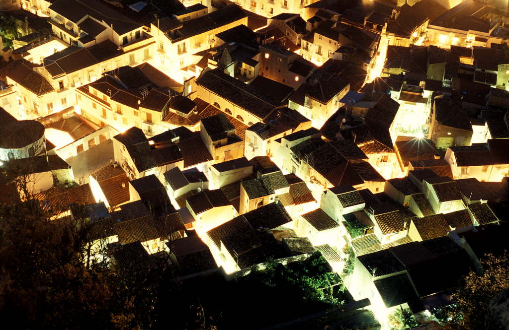 Illuminated rooftops of a town seen from above at night.