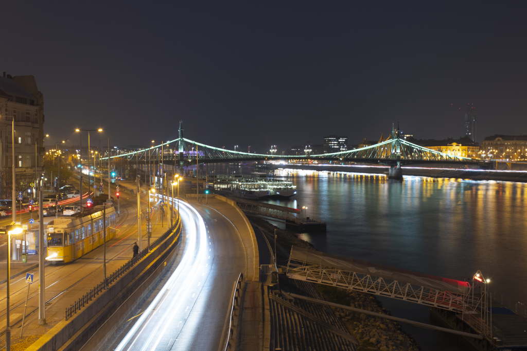 Riverside roadway and bridge at night with sweeping light trails.